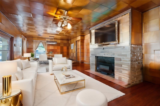 living room featuring ceiling fan, hardwood / wood-style flooring, and a stone fireplace