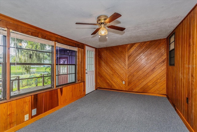 empty room featuring carpet floors, a textured ceiling, and wood walls