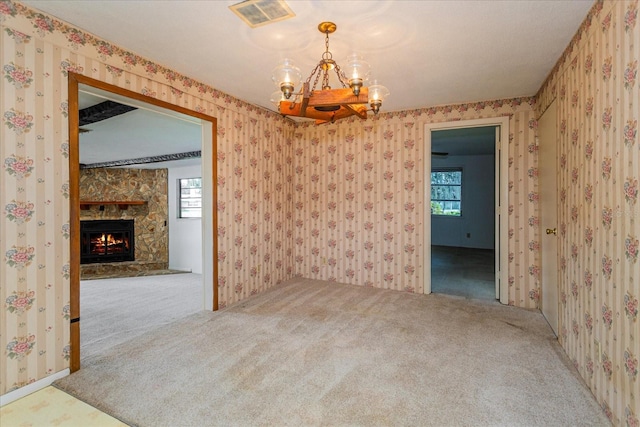 spare room with carpet floors, a stone fireplace, a notable chandelier, and a healthy amount of sunlight