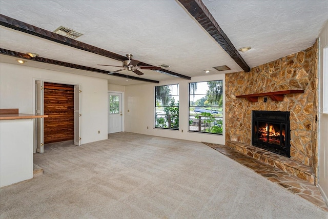 unfurnished living room featuring ceiling fan, beam ceiling, carpet, a fireplace, and a textured ceiling