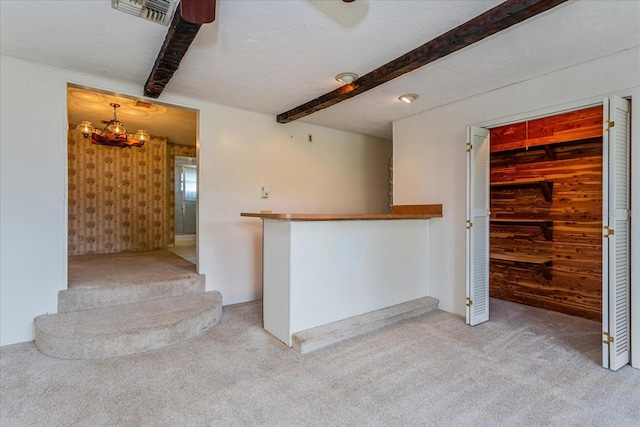 kitchen with a textured ceiling, light colored carpet, and beamed ceiling