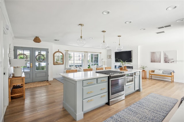 kitchen featuring stainless steel range with gas stovetop, hanging light fixtures, light wood-type flooring, ornamental molding, and french doors