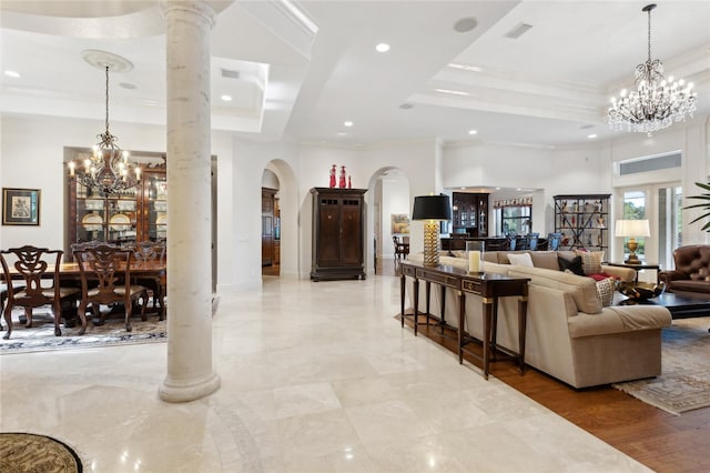 living area with crown molding, decorative columns, a tray ceiling, and a notable chandelier