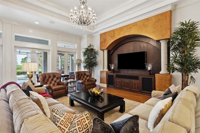 living area with decorative columns, ornamental molding, wood finished floors, a tray ceiling, and a chandelier