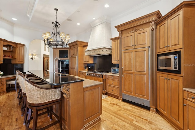 kitchen with light wood finished floors, ornamental molding, brown cabinets, stainless steel appliances, and premium range hood