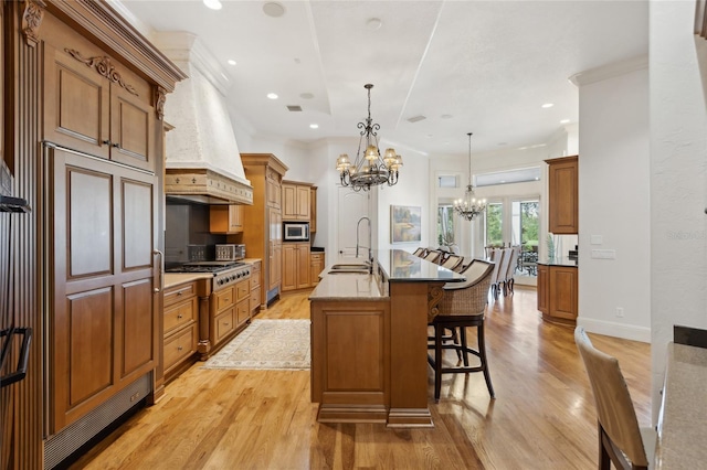 kitchen with custom range hood, appliances with stainless steel finishes, a kitchen breakfast bar, a notable chandelier, and a sink