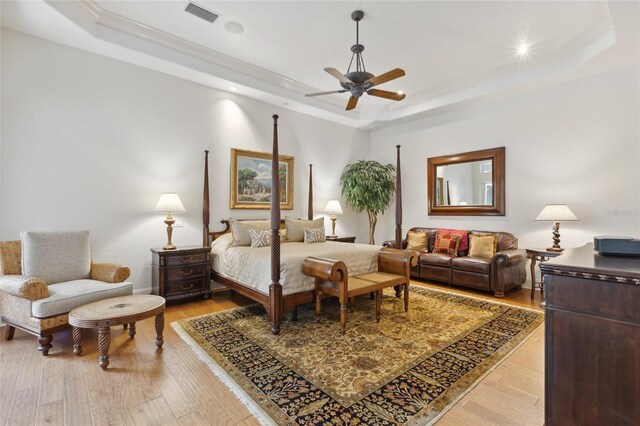 bedroom with a tray ceiling, visible vents, crown molding, and light wood-style flooring