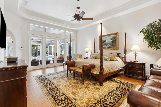 bedroom with arched walkways, access to exterior, a tray ceiling, french doors, and light wood-style floors