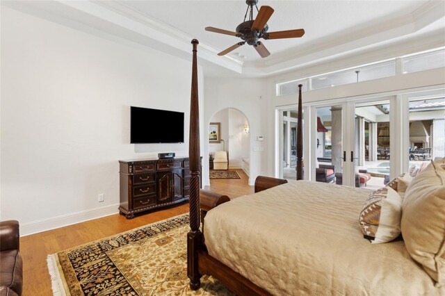 bedroom with arched walkways, a raised ceiling, ornamental molding, wood finished floors, and access to outside