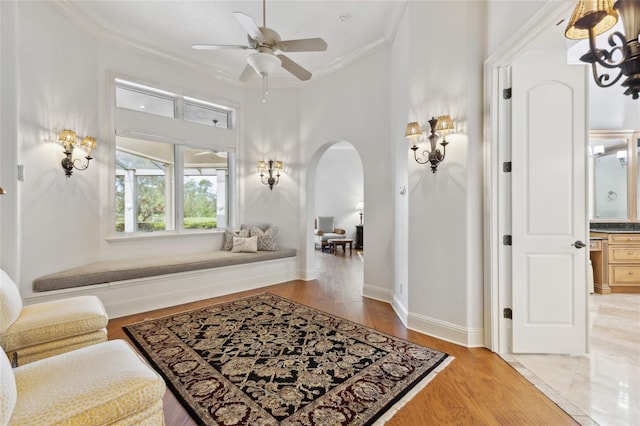 living area featuring light wood-style floors, arched walkways, crown molding, and baseboards