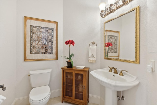 half bath with toilet, baseboards, and a sink