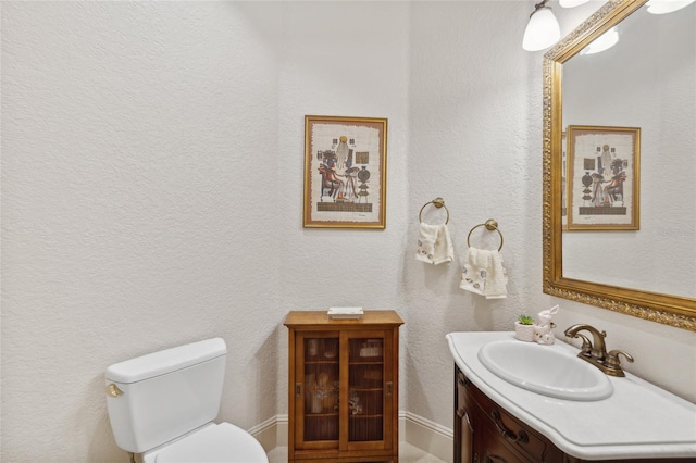 half bathroom featuring toilet, a textured wall, and vanity