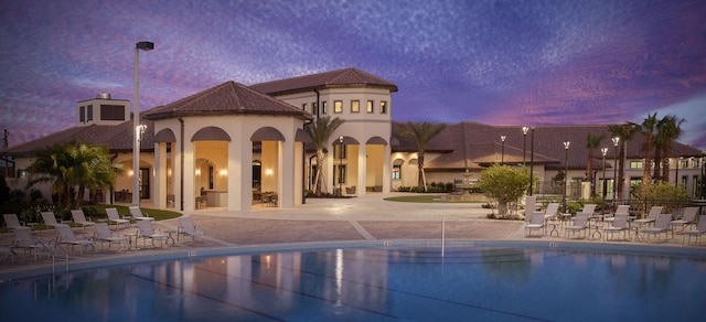 pool at dusk featuring a patio area and a community pool