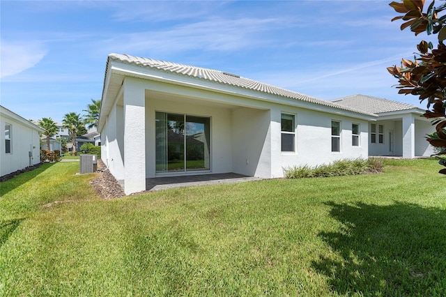 rear view of house with central air condition unit, a tiled roof, a lawn, and stucco siding