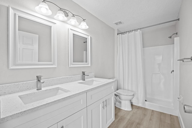 bathroom featuring hardwood / wood-style flooring, double vanity, a shower with curtain, toilet, and a textured ceiling