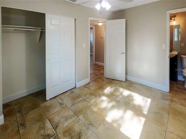 unfurnished bedroom featuring a closet, ensuite bathroom, light tile patterned floors, and ceiling fan