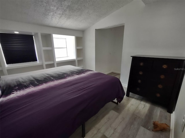 bedroom featuring light hardwood / wood-style floors, a textured ceiling, and lofted ceiling