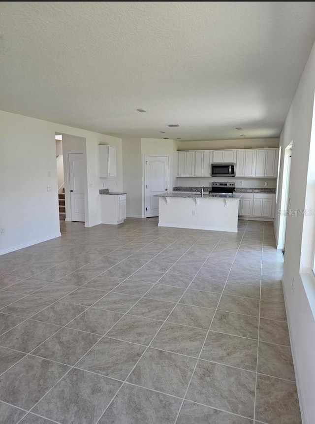 kitchen featuring stainless steel appliances, a textured ceiling, a breakfast bar, white cabinets, and a kitchen island with sink