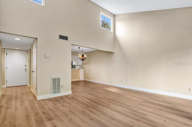 unfurnished living room featuring light wood-type flooring, a notable chandelier, and a high ceiling