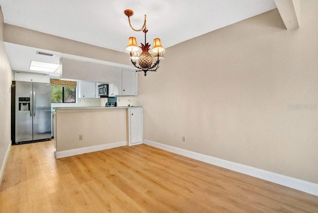 kitchen with white cabinetry, kitchen peninsula, appliances with stainless steel finishes, a chandelier, and light hardwood / wood-style flooring