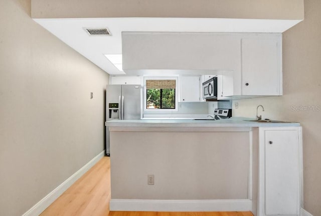 kitchen with stainless steel appliances, kitchen peninsula, sink, white cabinetry, and light hardwood / wood-style flooring