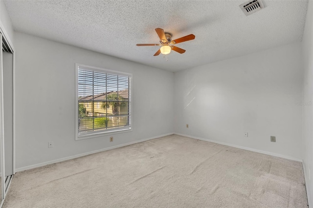 empty room featuring ceiling fan, light carpet, and a textured ceiling