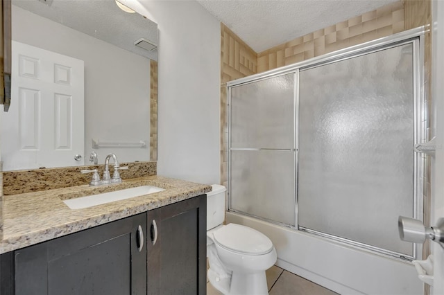 full bathroom featuring combined bath / shower with glass door, vanity, a textured ceiling, tile patterned floors, and toilet