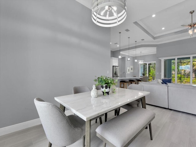 dining space with ceiling fan with notable chandelier, a tray ceiling, ornamental molding, and sink