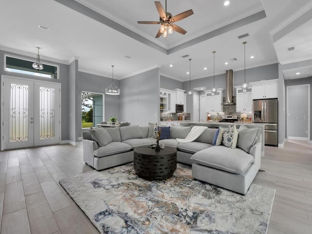 living room with light wood-type flooring, ornamental molding, ceiling fan, and a raised ceiling