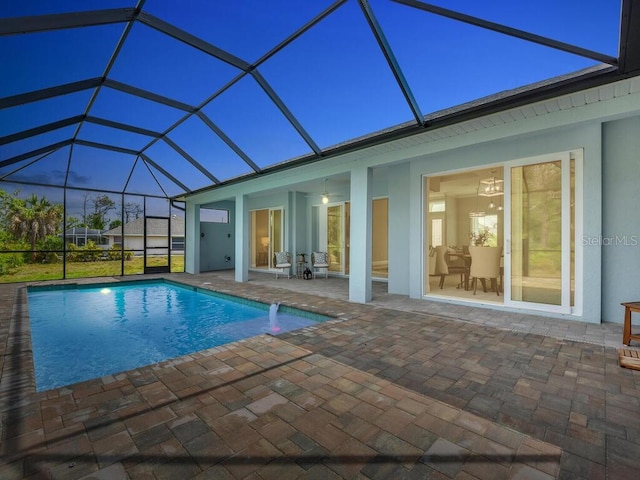 pool at dusk with pool water feature, a lanai, and a patio area