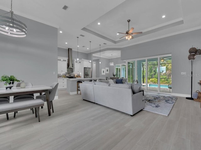 living room with a towering ceiling, light hardwood / wood-style flooring, a raised ceiling, crown molding, and ceiling fan with notable chandelier