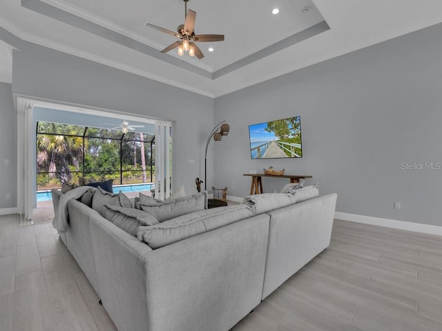 living room featuring a tray ceiling, ornamental molding, ceiling fan, and light hardwood / wood-style floors