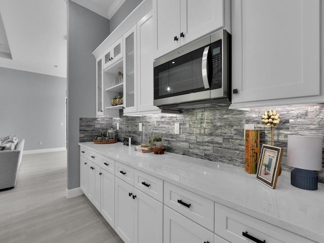 kitchen with tasteful backsplash, white cabinetry, crown molding, and light stone countertops