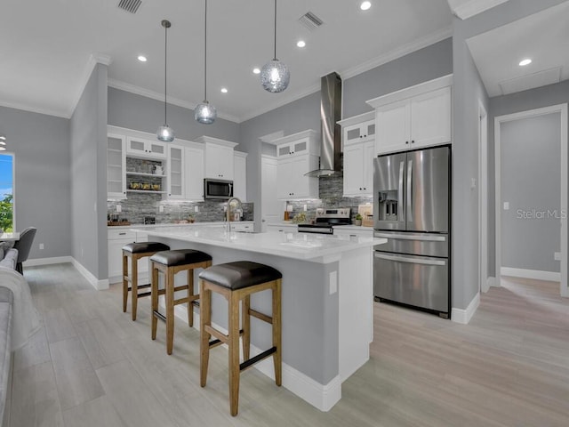 kitchen with white cabinetry, hanging light fixtures, a large island with sink, appliances with stainless steel finishes, and wall chimney range hood