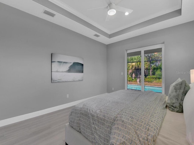 bedroom with ceiling fan, access to outside, wood-type flooring, and a raised ceiling