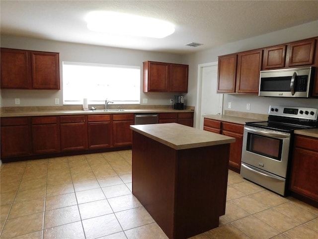 kitchen with light tile patterned floors, stainless steel appliances, a kitchen island, and sink