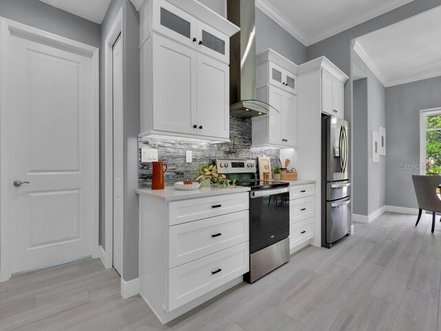 kitchen with crown molding, wall chimney range hood, white cabinets, backsplash, and stainless steel appliances