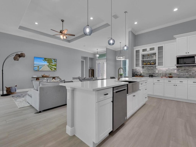 kitchen with appliances with stainless steel finishes, sink, decorative backsplash, light wood-type flooring, and a tray ceiling