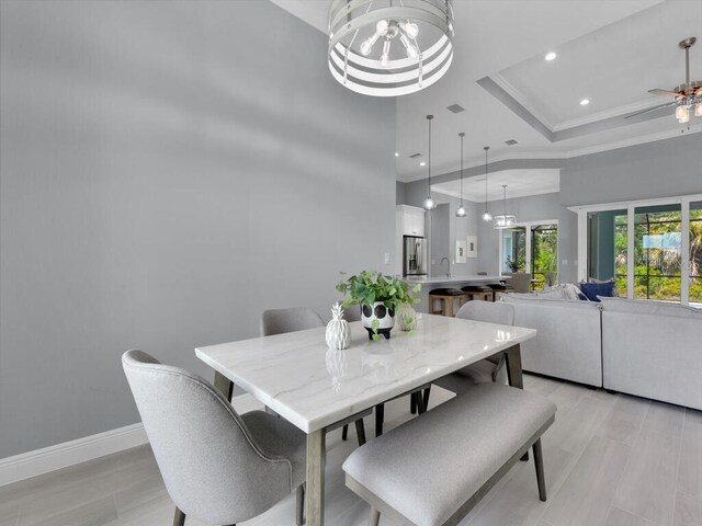 dining room featuring a tray ceiling, ceiling fan with notable chandelier, sink, light hardwood / wood-style flooring, and a towering ceiling