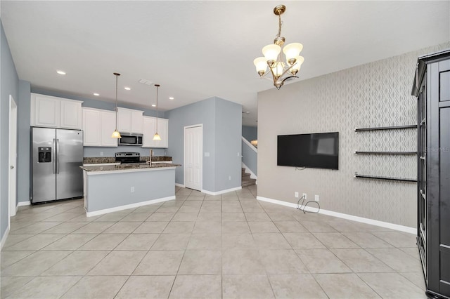 kitchen with a kitchen island with sink, stainless steel appliances, light stone counters, white cabinets, and pendant lighting