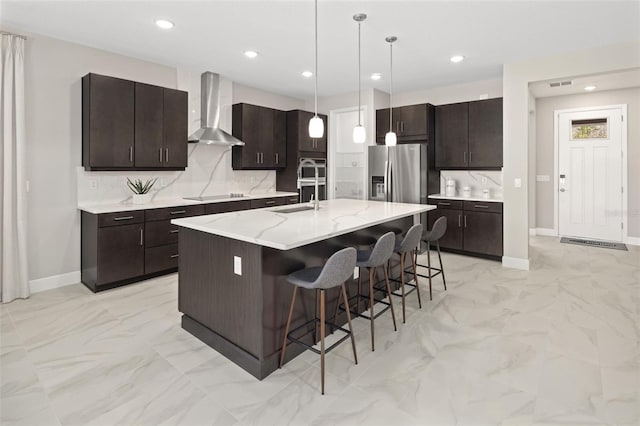 kitchen featuring wall chimney exhaust hood, a breakfast bar, sink, appliances with stainless steel finishes, and a kitchen island with sink