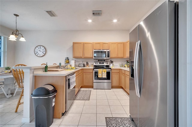 kitchen featuring stainless steel appliances, light brown cabinetry, hanging light fixtures, and light tile patterned floors