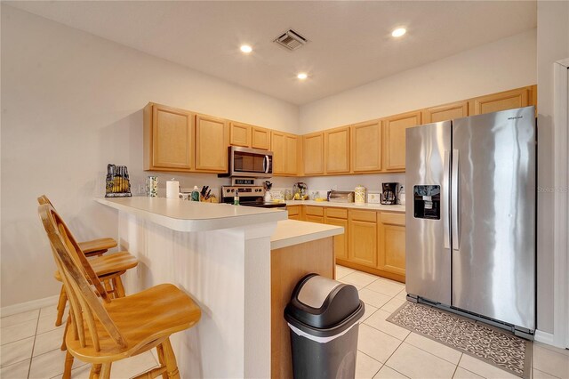 kitchen with appliances with stainless steel finishes, light brown cabinetry, a breakfast bar area, light tile patterned floors, and kitchen peninsula