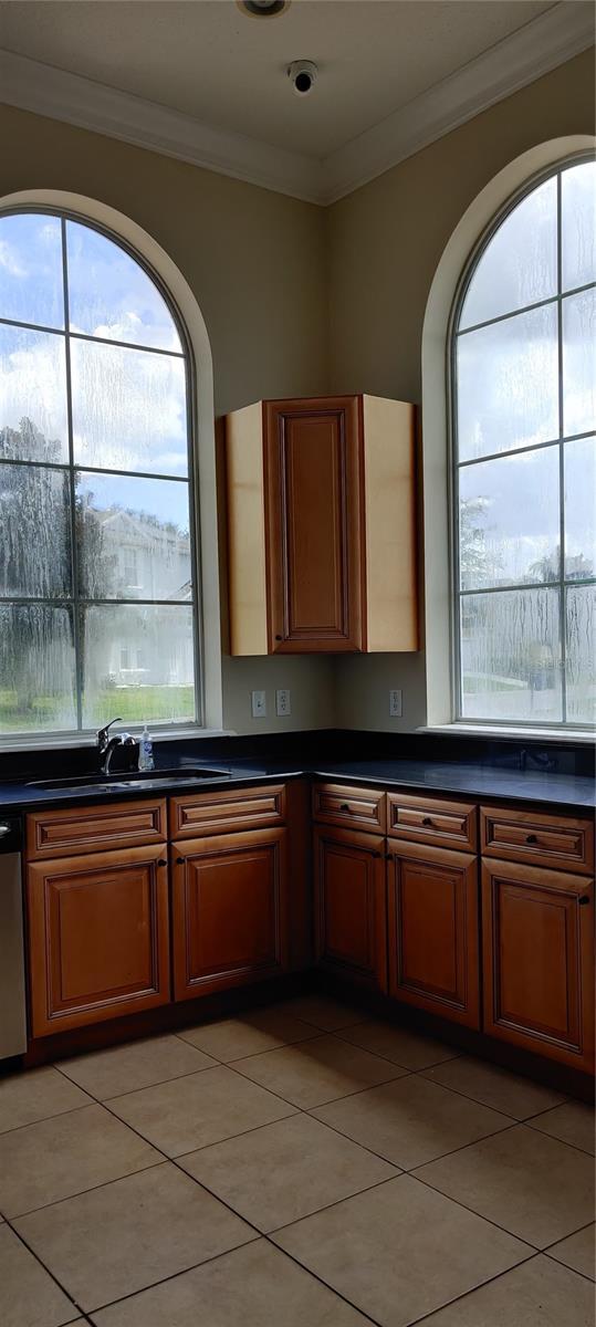 kitchen featuring crown molding, stainless steel dishwasher, sink, and light tile patterned floors