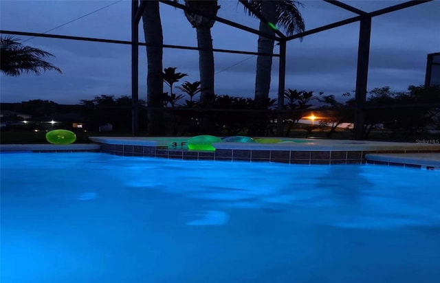 pool at dusk featuring a lanai and pool water feature