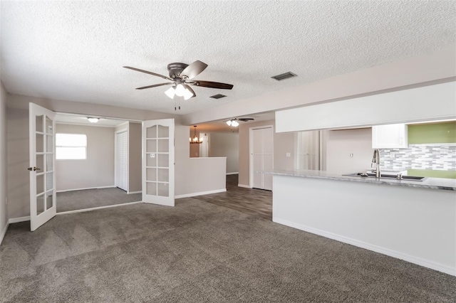 unfurnished living room with sink, french doors, a textured ceiling, and dark colored carpet