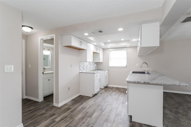 kitchen with sink, dark wood-type flooring, white cabinetry, kitchen peninsula, and a raised ceiling