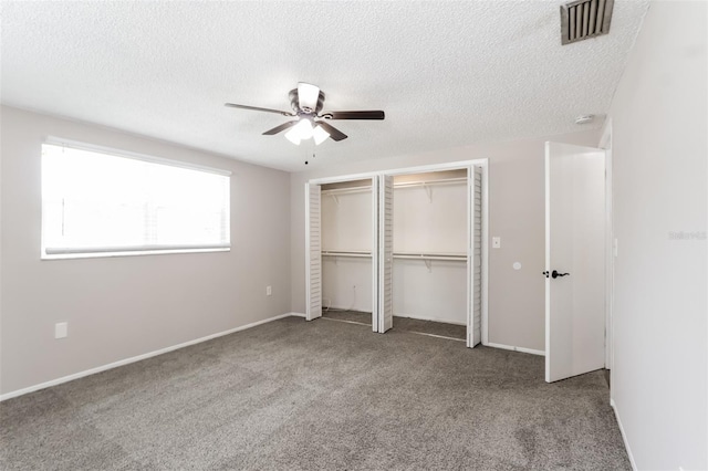 unfurnished bedroom featuring ceiling fan, a textured ceiling, carpet floors, and multiple closets