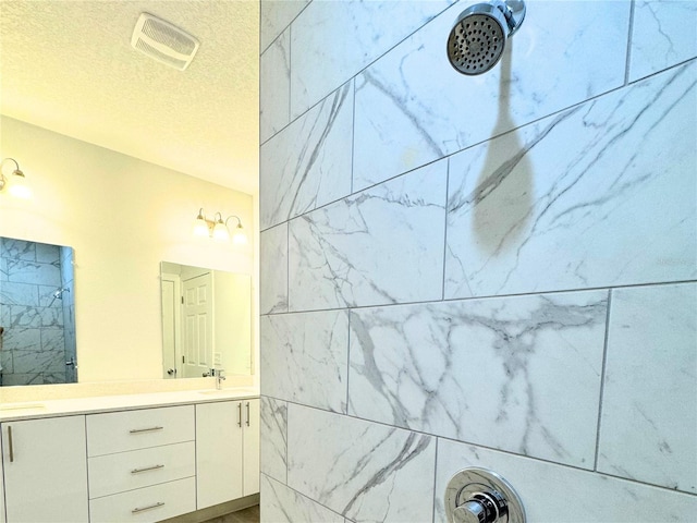 bathroom featuring tiled shower, vanity, and a textured ceiling