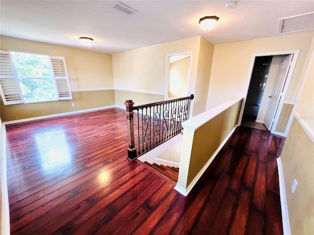 hall with baseboards, visible vents, wood finished floors, and an upstairs landing